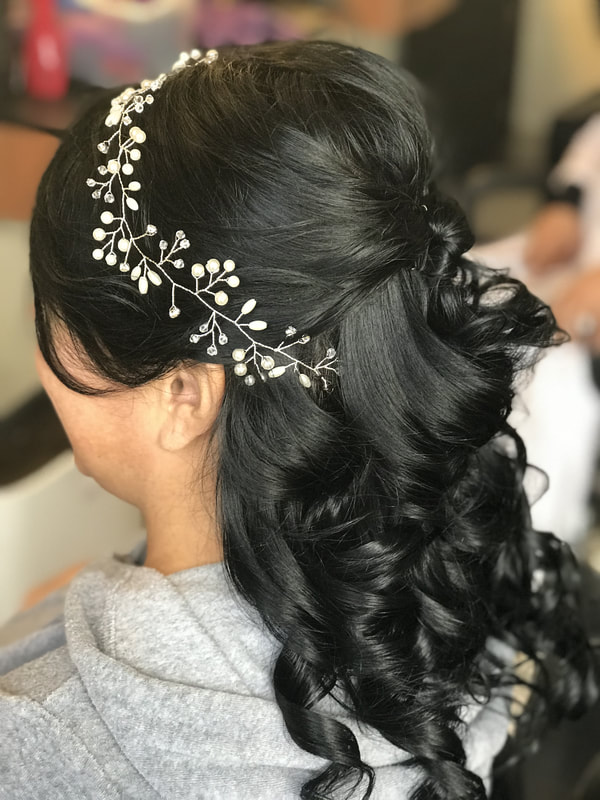Picture of client with dark brown hair pulled back and curled she has a flowery hair clip 